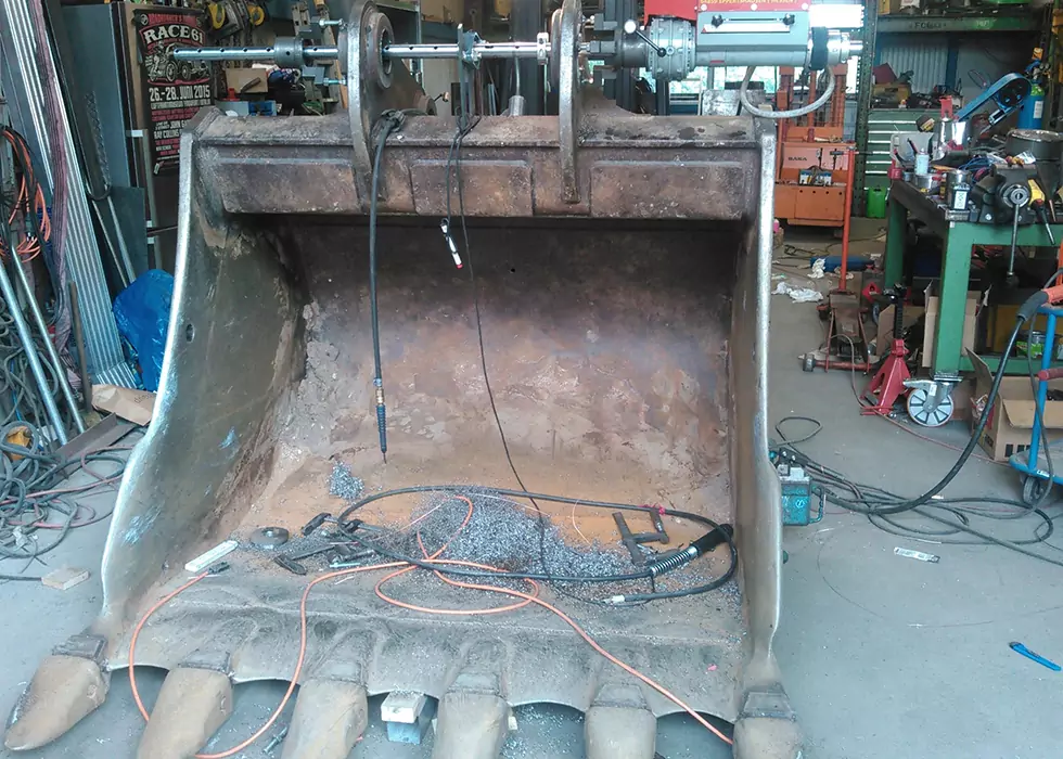 Große Baggerschaufel liegt abmontiert auf dem Werkstattboden in einer Werkstatt